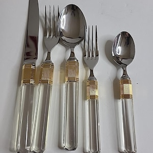 May include: A set of five pieces of silverware: a knife, two forks, and two spoons. The silverware has clear, faceted handles with gold-colored bands at the top and bottom. The knife and silverware blades are silver.