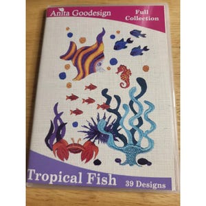 May include: A rectangular Anita Goodesign Full Collection DVD case titled Tropical Fish 39 Designs. The cover features embroidered-style illustrations of a large striped fish, a seahorse, a crab, small red fish, and blue sea plants on white.