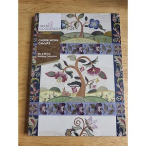 May include: A rectangular Anita Goodesign Crewelwork Canvas Mix & Match Quilting Collection package featuring embroidered landscape scenes with trees, flowers, and a small animal. The design includes purple, green, and brown tones on a white background.