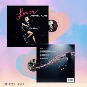 May include: A vinyl record set featuring the album "Lover Live From Paris." The album cover shows a singer with a guitar. The set includes two heart-shaped vinyl records, one pink and yellow, the other blue and pink. The album title is in pink glitter.