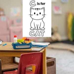 May include: A black and white illustration of a cat with the text "C is for CAT". The image is on a white background. A blue lunchbox, a red chair, and a wooden table are in the foreground.