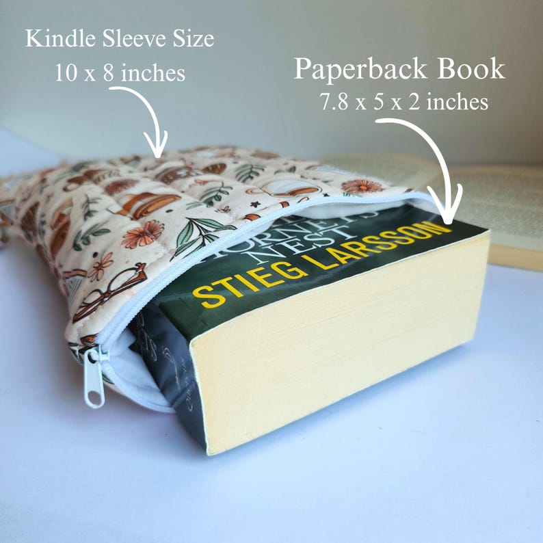 May include: A quilted fabric sleeve with a cream background and a pattern of brown coffee cups, glasses, and flowers. The sleeve measures 10 x 8 inches and contains a paperback book titled Hornet's Nest by Stieg Larsson, measuring 7.8 x 5 x 2 inches.