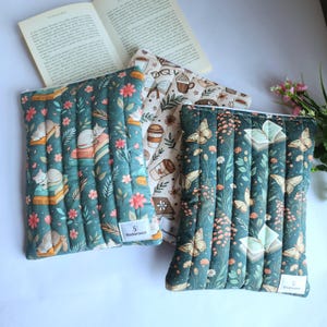 May include: Three rectangular quilted fabric pouches with zippered closures. One pouch features a dark green background with cats and books, another has a cream background with coffee cups and books, and the third has a dark green background with butterflies and books.