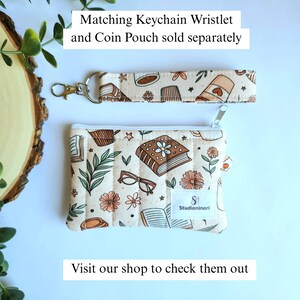 May include: A quilted fabric coin pouch and a matching keychain wristlet featuring a cream background with a repeating pattern of books, flowers, glasses, and coffee cups. The pouch has a white zipper and a label with the text Studioninori.