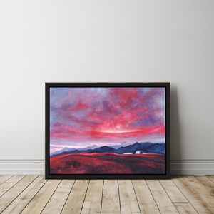 May include: A framed landscape painting featuring a vibrant sunset with shades of red, pink, and purple in the sky. Dark blue mountains and a reddish-brown foreground complete the scene. The artwork is in a black frame.