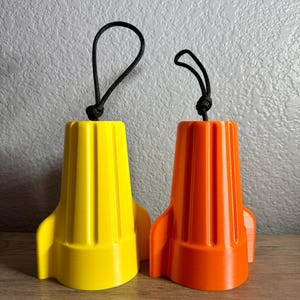 May include: Two plastic rocket-shaped bottle stoppers, one yellow and one orange, with black rope handles.