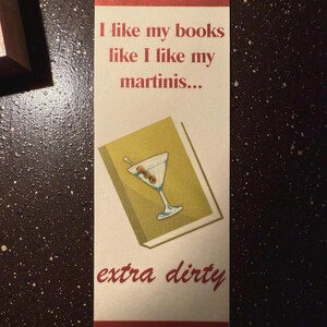 May include: A white bookmark with red and green stripes. The bookmark features a martini glass with olives and the text "I like my books like I like my martinis... extra dirty".