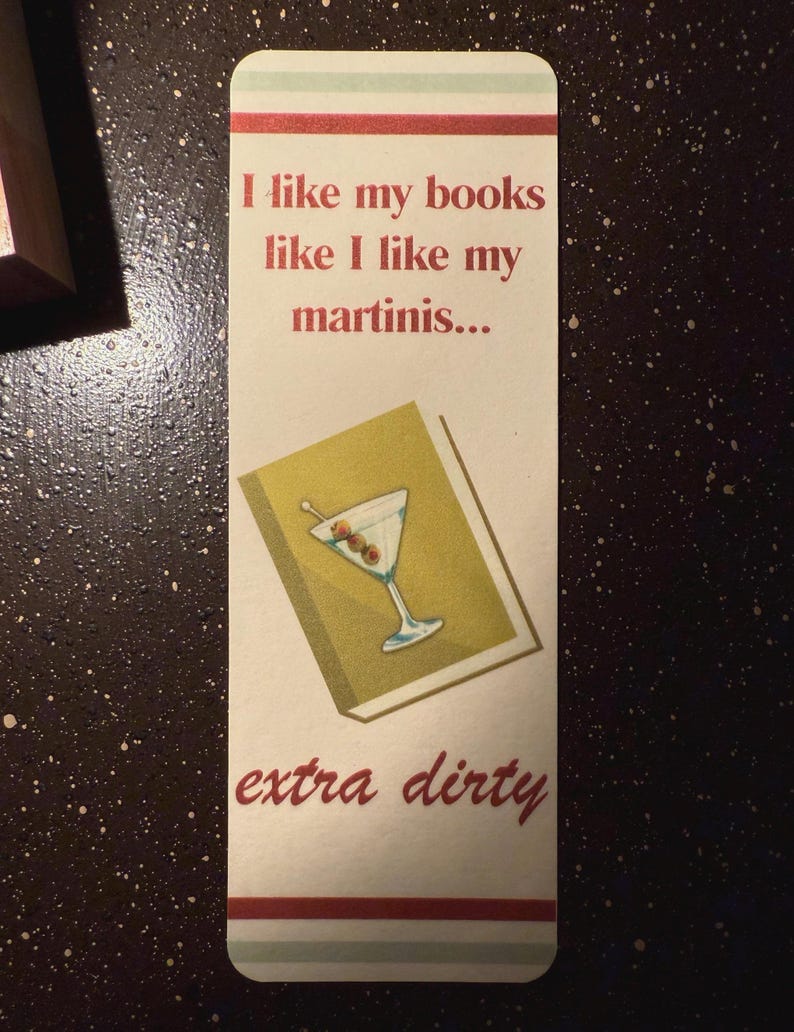 May include: A white bookmark with red and green stripes. The bookmark features a martini glass with olives and the text "I like my books like I like my martinis... extra dirty".