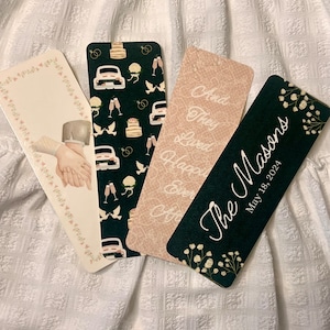 May include: Four wedding themed bookmarks. One bookmark features a couple's hands holding each other, another has a black background with white doves, wedding rings, and a car, another has a pink background with the text "And they lived happily ever after", and the last bookmark has a black background with white flowers and the text "The C. Masons May 18, 2024".