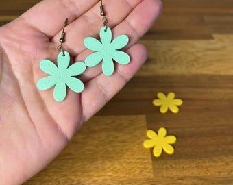 May include: A pair of mint green flower-shaped earrings with bronze-colored hooks. Two yellow flower-shaped objects are on a wooden surface. The image also contains the text "3D PRINTING FILES | STL".