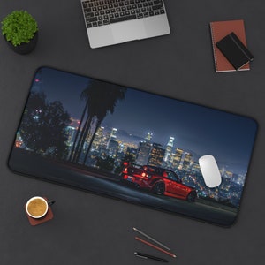 May include: A red sports car drives through a city at night. The car is driving on a road with a cityscape in the background. The city is lit up with lights. The car is a popular model for car enthusiasts.