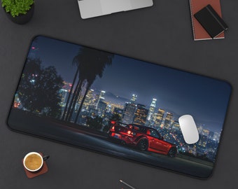 May include: A red sports car drives through a city at night. The car is driving on a road with a cityscape in the background. The city is lit up with lights. The car is a popular model for car enthusiasts.