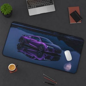 May include: A purple sports car mousepad with a black border. The car is reflected in the water, creating a mirrored image. A white mouse, a cup of coffee, and a laptop are also visible on the black surface.