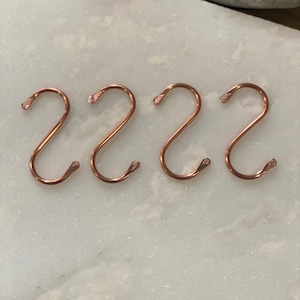 May include: Four rose gold S-shaped hooks. The hooks are made of metal and have a smooth, polished finish.