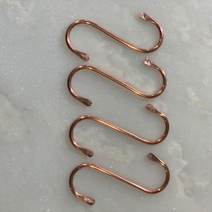 May include: Four copper S-shaped hooks, each with a rounded end. The hooks are arranged in a vertical stack, with the top hook at the top of the image and the bottom hook at the bottom of the image.