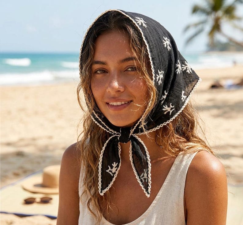 May include: A black headscarf featuring a white embroidered pattern of small coral-like shapes. The triangular fabric is tied under the chin and finished with a delicate white scalloped lace trim along all edges, creating a textured appearance.