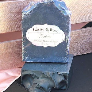 May include: A black charcoal soap bar with a white label that reads "Lustre & Rose Charcoal Artisan Natural Soap 4.5 oz Bar".