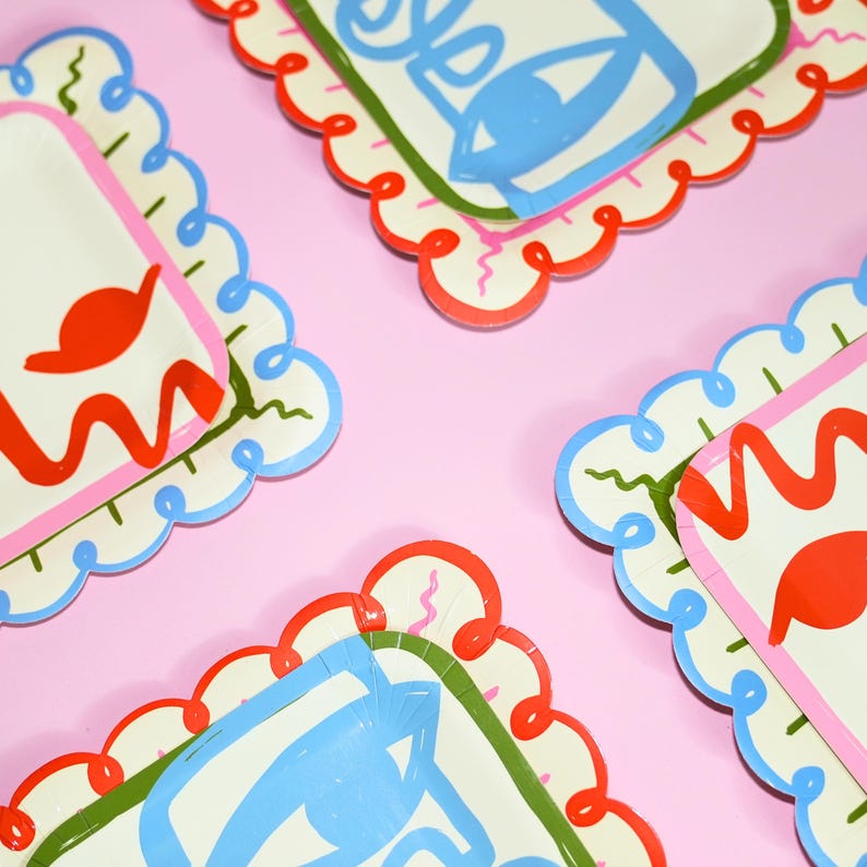 May include: A set of square paper plates with scalloped edges featuring a colorful abstract design. The plates display bold red, blue, and green line art patterns on a cream background, with some plates showing a stylized eye motif in blue.