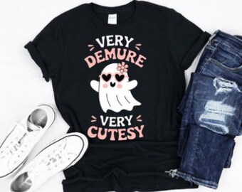 Könnte beinhalten: Schwarzes T-Shirt mit einem rosa Geist, der eine Sonnenbrille und eine Blume trägt. Der Text "Very Demure Very Cutesy" ist auf das Shirt gedruckt.