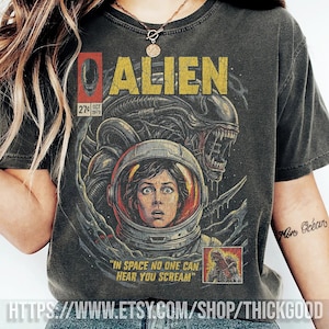 Puede incluir: Camiseta gris oscuro con un diseño gráfico vintage de la película "Alien". El diseño incluye la palabra "ALIEN" en amarillo, una imagen desgastada de una mujer con casco espacial y la frase "IN SPACE NO ONE CAN HEAR YOU SCREAM."