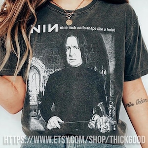 May include: Dark gray t-shirt featuring a graphic of a person and the text "NIN nine inch nails snape like a hole!". The shirt has a vintage, worn look. The Etsy shop URL is visible at the bottom of the shirt.