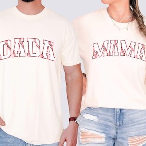 May include: Two white t-shirts with red baseball-themed text. One shirt says "DADA" and the other says "MAMA".