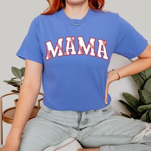 May include: A royal blue t-shirt with a white baseball-themed "MAMA" graphic. The letters are outlined in red and have a baseball stitch design.