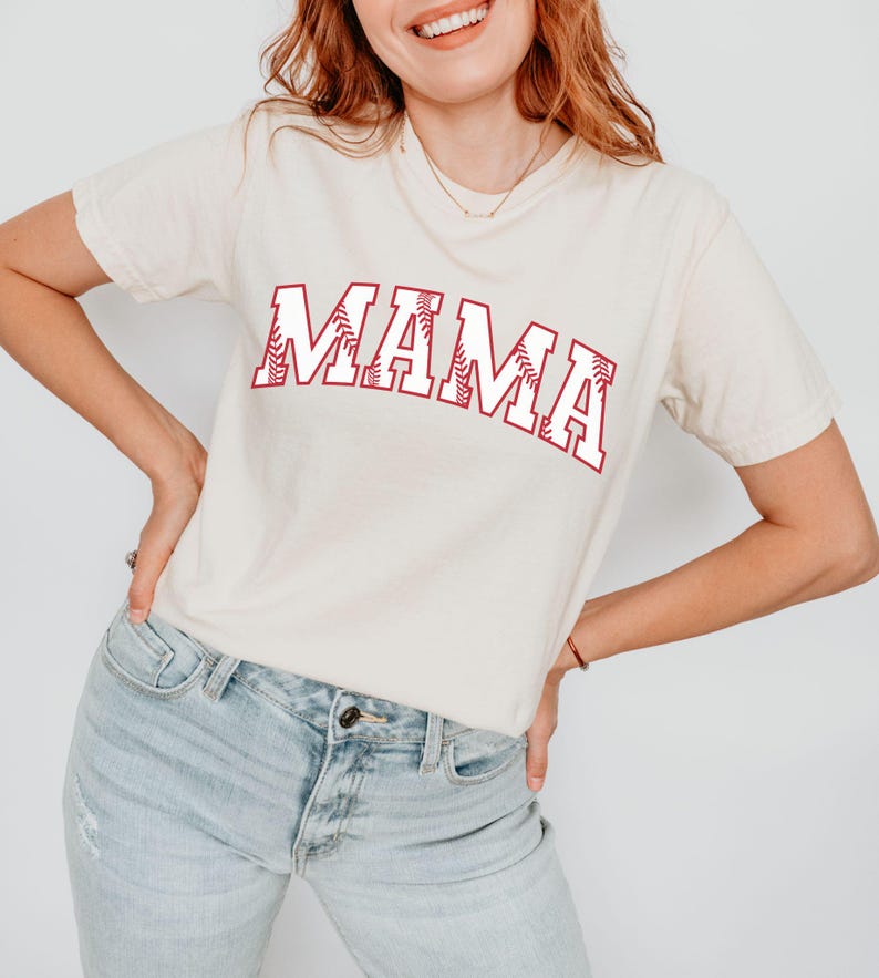 May include: A white t-shirt with the word "MAMA" printed in red with a baseball stitch design.