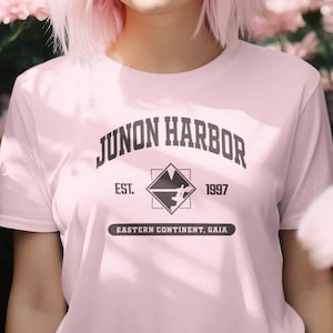 May include: Pink t-shirt with a black graphic print that says "Junon Harbor Est. 1997 Eastern Continent, Gaia"
