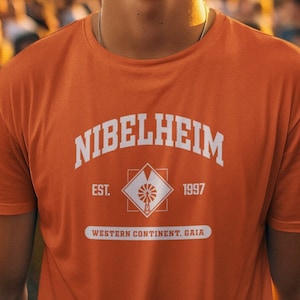 Könnte beinhalten: Ein orangefarbenes T-Shirt mit kurzen Ärmeln, das den weißen Schriftzug NIBELHEIM EST. 1997, ein zentrales Rautenmotiv mit einem Windmühlensymbol und den Text WESTERN CONTINENT, GAIA auf einem weißen horizontalen Banner auf der Brust zeigt.