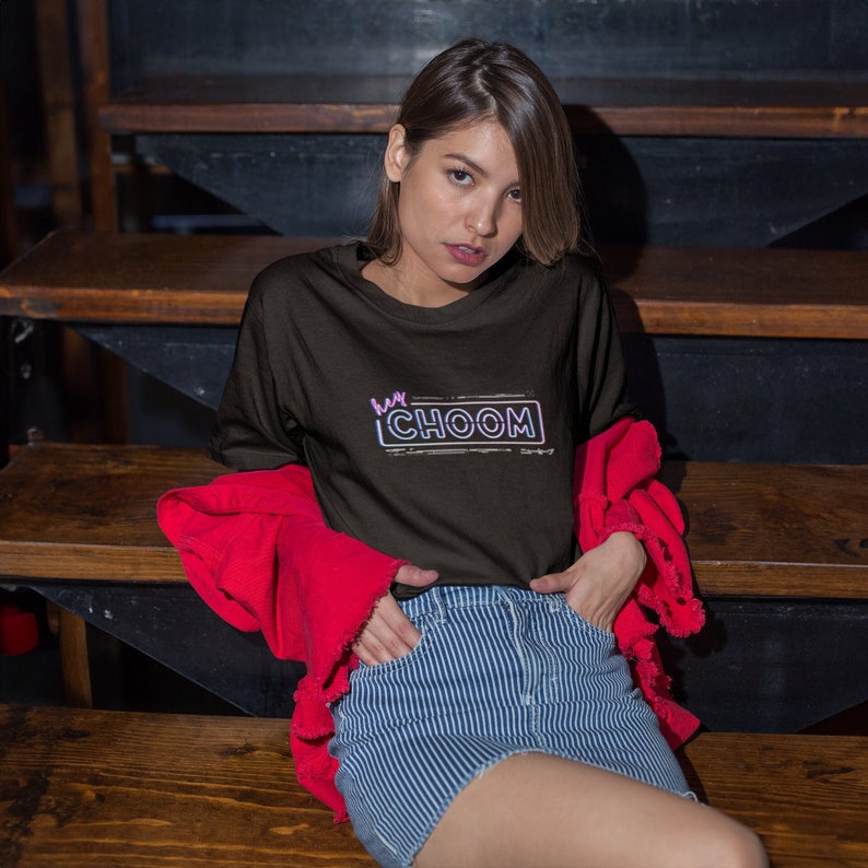 Woman sitting on wooden bleachers wearing a black Cyberpunk 2077 Hey Choom Unisex Oversized T-Shirt by New Save.
