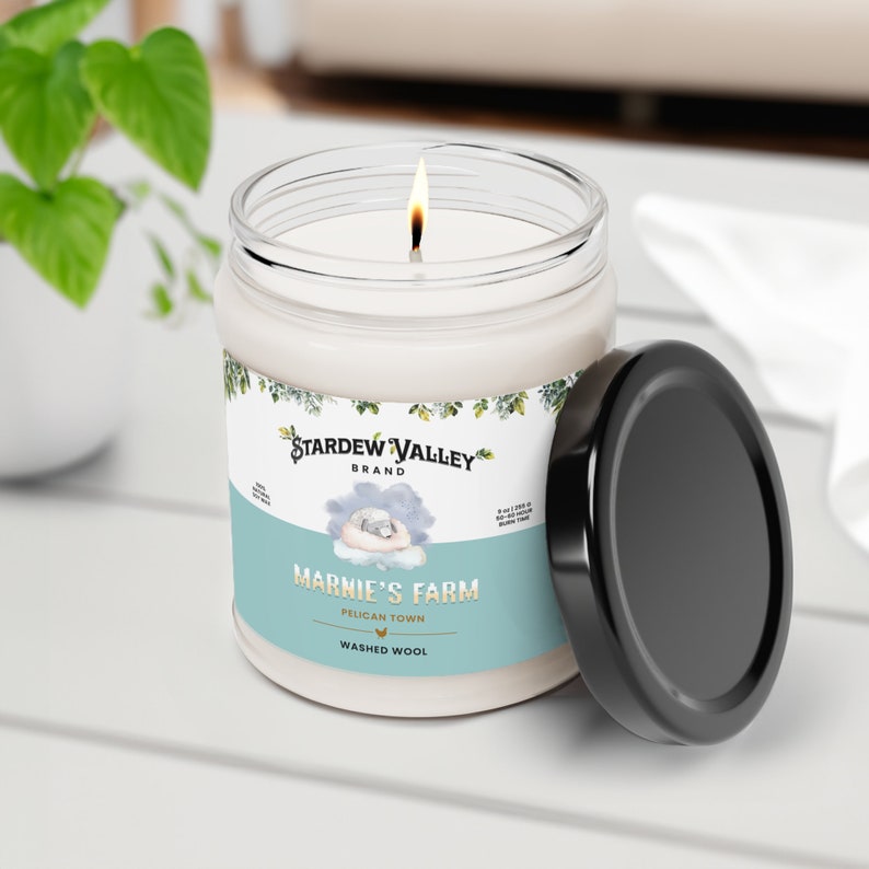 May include: A lit candle in a glass jar with a black lid. The label reads "Stardew Valley Brand" and "Marnie's Farm, Pelican Town, Washed Wool." The candle is 3 inches in diameter and has a burn time of 50 hours.
