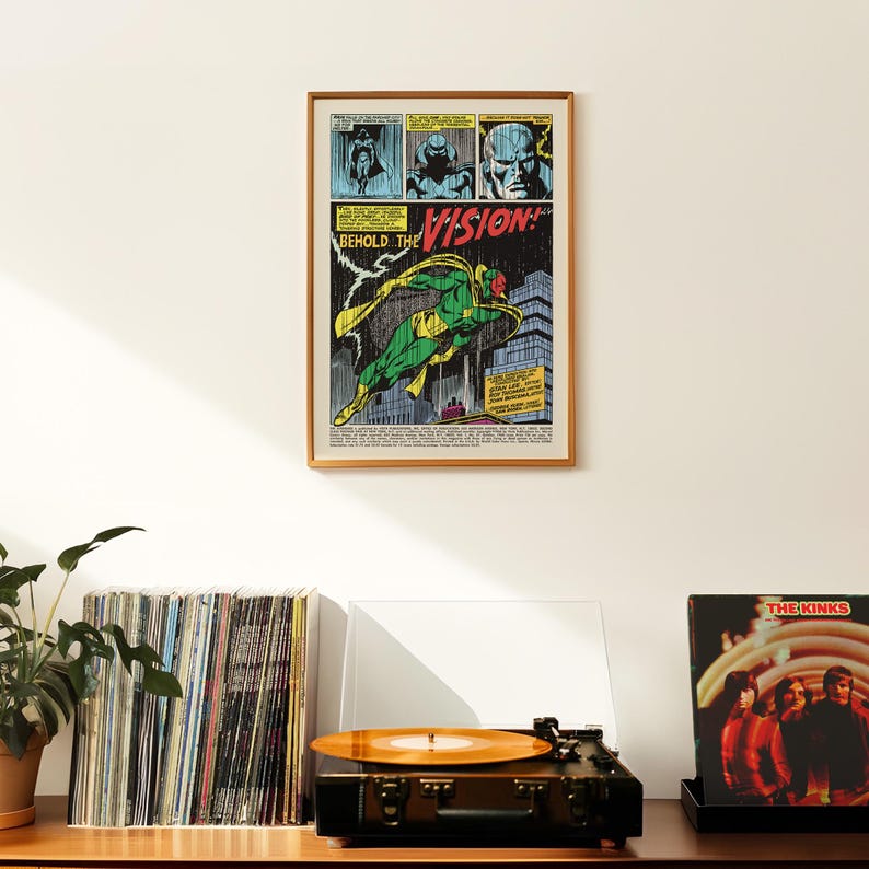 May include: A framed comic book page featuring the character Vision in a dynamic pose, with the text "BEHOLD THE VISION!" in bold letters. The artwork is in vibrant colors, set against a white wall. A record player and vinyl records are in the foreground.