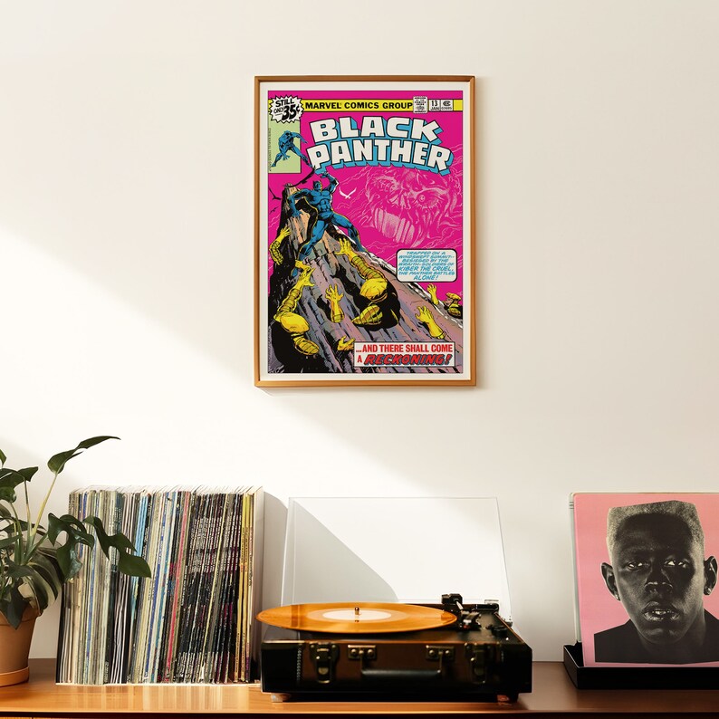 May include: A framed comic book cover featuring Black Panther in a blue suit, standing on a rocky cliff. The cover is pink with the title "Black Panther" in white letters. The text "And there shall come a reckoning!" is at the bottom of the cover.