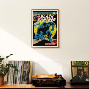 May include: A vintage comic book cover featuring the Black Panther in a black and blue costume, with the title "Jungle Action Featuring The Black Panther" in green and yellow text. The cover is framed in a gold frame and hanging on a white wall.