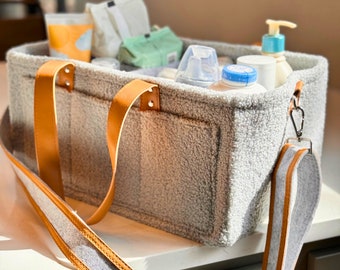 May include: A gray and white fuzzy tote bag with brown leather handles and a long strap. The bag is filled with various baby items, including bottles, lotion, and wipes.