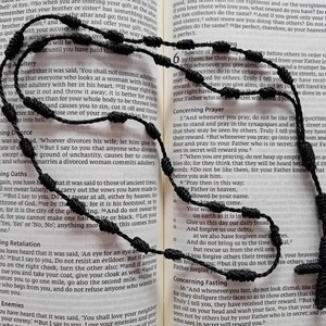 May include: A black rosary with a wooden cross, lying on an open book with text about prayer and forgiveness. The book is titled "Concerning Prayer" and "Concerning Fasting".