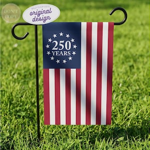 May include: A rectangular garden flag hanging on a black metal stand. The flag features a blue canton with a circle of thirteen white stars surrounding the white text 250 YEARS. The remaining area consists of alternating vertical red and white stripes.