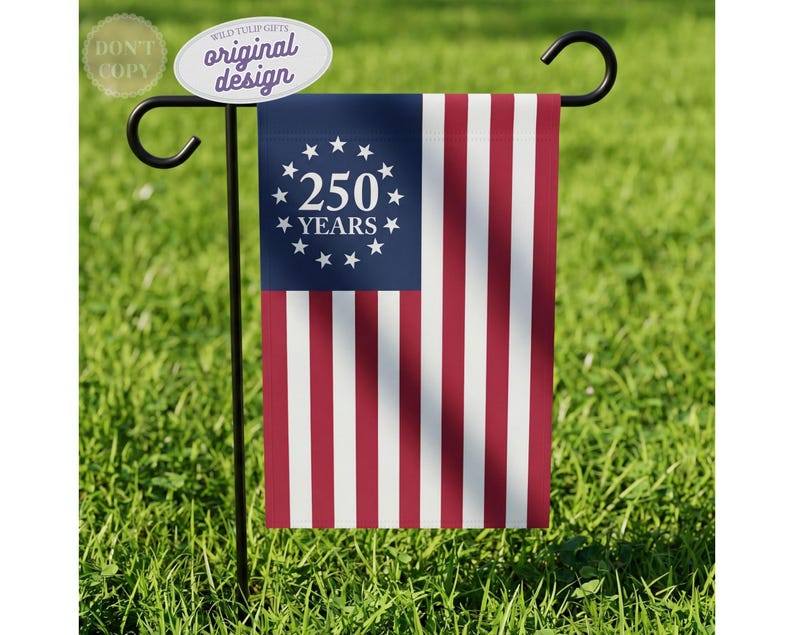 May include: A rectangular garden flag hanging on a black metal stand. The flag features a blue canton with a circle of thirteen white stars surrounding the white text 250 YEARS. The remaining area consists of alternating vertical red and white stripes.