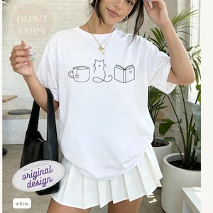 May include: White t-shirt with a black line drawing of a teacup, cat, and book. The shirt has the text "DON'T COPY" and "original design". The shirt is paired with a white pleated skirt and a black shoulder bag.