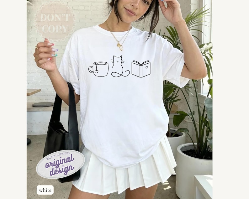 May include: White t-shirt with a black line drawing of a teacup, cat, and book. The shirt has the text "DON'T COPY" and "original design". The shirt is paired with a white pleated skirt and a black shoulder bag.