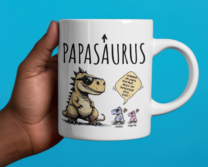 Puede incluir: Taza de cer&aacute;mica blanca con la palabra "PAPASAURUS" y una ilustraci&oacute;n de un dinosaurio con gafas de sol. La taza tambi&eacute;n presenta dos dinosaurios m&aacute;s peque&ntilde;os y texto en un bocadillo.