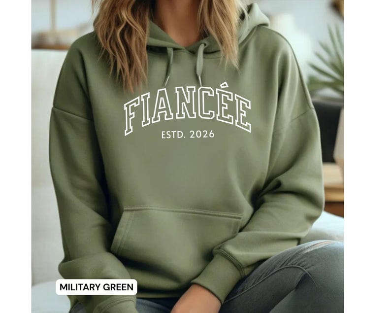 May include: Military green hoodie with the word "FIANC&Eacute;E" in white, arched across the chest, with "ESTD. 2026" below. The hoodie has a drawstring hood and a front pocket.