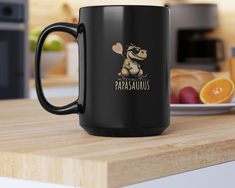 Puede incluir: Taza de cer&aacute;mica negra con un dinosaurio de dibujos animados con gafas de sol y un globo en forma de coraz&oacute;n. El texto "PAPASAURUS" est&aacute; impreso debajo en color dorado. La taza tiene un asa grande y curvada.
