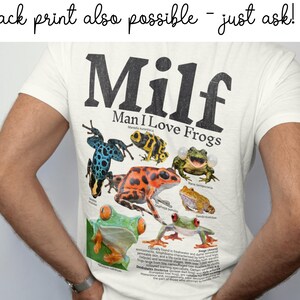 May include: Cream-colored t-shirt with the text "Milf Man I Love Frogs" in black. The shirt features a colorful graphic of various frog species. The phrase "back print also possible - just ask!" is at the top.