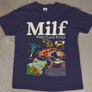 May include: Navy blue t-shirt featuring the text "Milf Man I Love Frogs" in white, with various colorful frog illustrations. The shirt includes scientific names and descriptions of the frogs.
