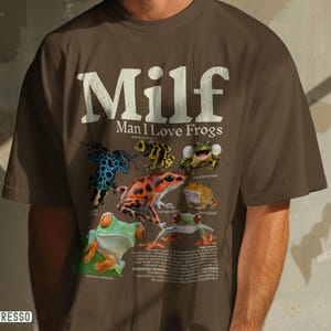 May include: Espresso-colored t-shirt with the text "Milf Man I Love Frogs" in white. The shirt features colorful illustrations of various frog species. The word "Espresso" is printed in a white rectangle at the bottom left.