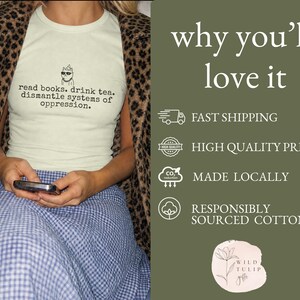 May include: A light green t-shirt featuring a graphic of a cat wearing sunglasses and a party hat, with the text: read books. drink tea. dismantle systems of oppression. The shirt is worn under a brown and black leopard print jacket and a blue skirt.