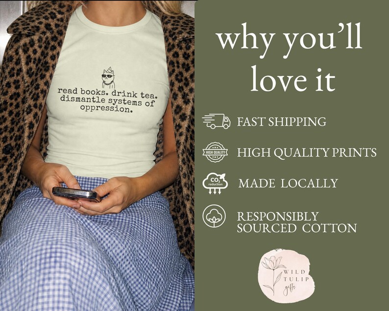 May include: A light green t-shirt featuring a graphic of a cat wearing sunglasses and a party hat, with the text: read books. drink tea. dismantle systems of oppression. The shirt is worn under a brown and black leopard print jacket and a blue skirt.