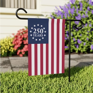 May include: A rectangular garden flag featuring a blue canton with a circle of thirteen white stars surrounding the white text 250 YEARS, and vertical red and white stripes. The flag hangs from a black metal garden stake stand.